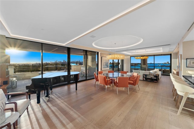 dining room featuring expansive windows, light hardwood / wood-style flooring, an inviting chandelier, and a tray ceiling