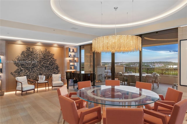 dining area with a raised ceiling, light hardwood / wood-style floors, and a notable chandelier