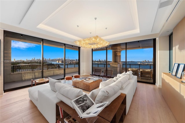 living room with a notable chandelier, floor to ceiling windows, a raised ceiling, and light wood-type flooring