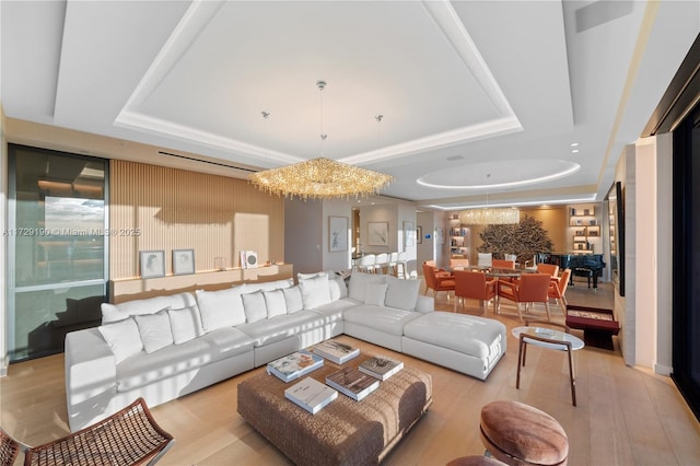 living room with a tray ceiling, a chandelier, and light hardwood / wood-style flooring