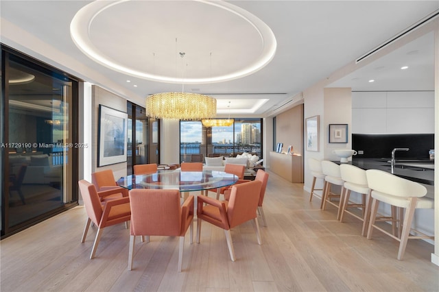 dining area featuring a raised ceiling, light hardwood / wood-style floors, and a notable chandelier