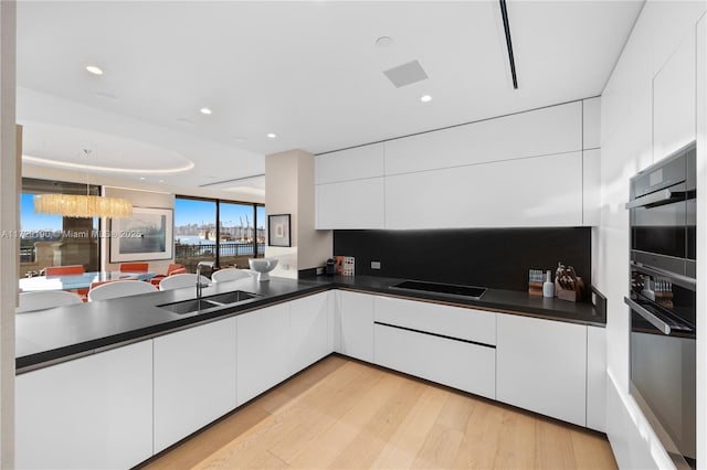 kitchen with black electric stovetop, light hardwood / wood-style floors, sink, and white cabinets