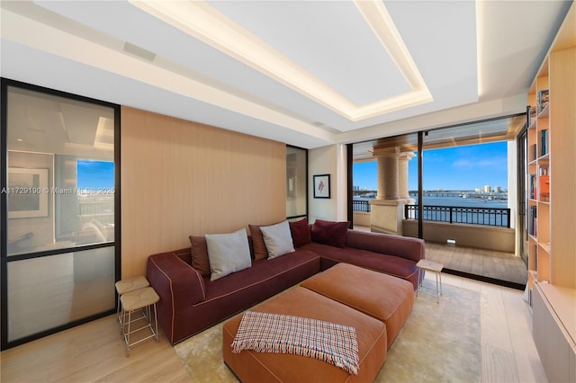 living room featuring light wood-type flooring, ornate columns, and a water view