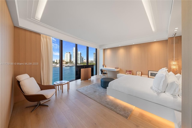 bedroom with expansive windows, a water view, access to exterior, and light hardwood / wood-style flooring