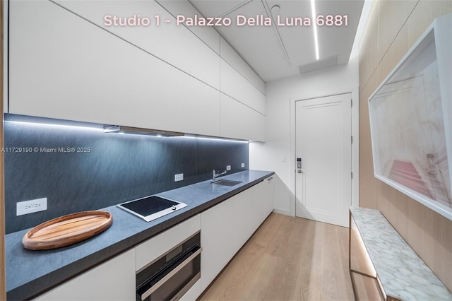 kitchen with sink, light wood-type flooring, white cabinets, oven, and backsplash