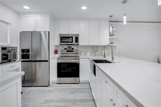 kitchen with sink, appliances with stainless steel finishes, hanging light fixtures, white cabinets, and light wood-type flooring