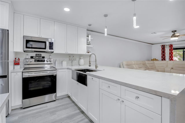 kitchen with appliances with stainless steel finishes, decorative light fixtures, white cabinets, light hardwood / wood-style floors, and kitchen peninsula