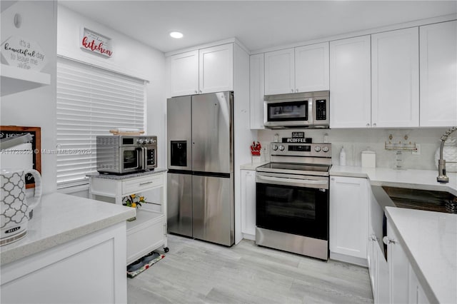 kitchen with light wood-style flooring, recessed lighting, white cabinetry, appliances with stainless steel finishes, and light stone countertops