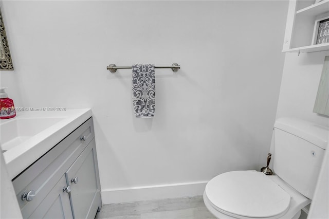 half bathroom featuring toilet, vanity, and baseboards