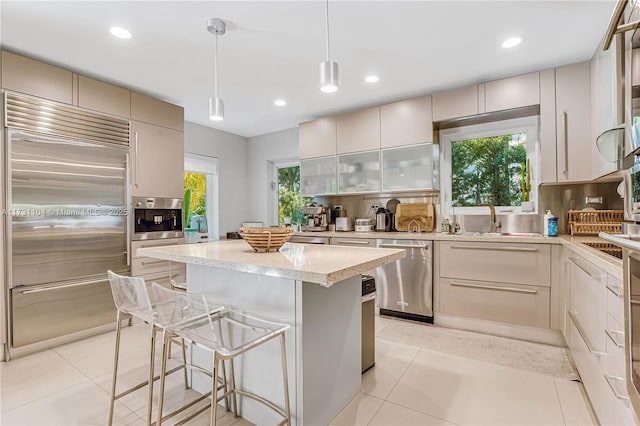 kitchen with light tile patterned flooring, light stone countertops, a sink, stainless steel appliances, and a kitchen island