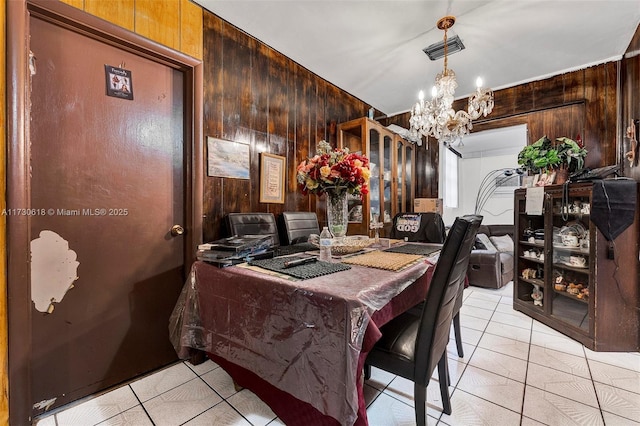 dining space with wood walls, a chandelier, and light tile patterned flooring