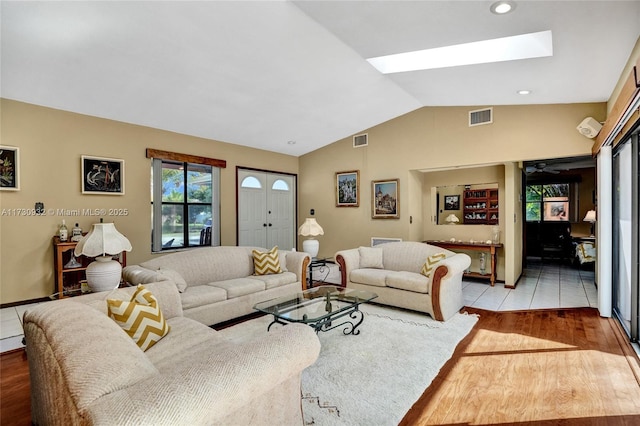 living room featuring vaulted ceiling with skylight and light wood-type flooring