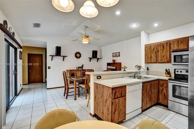 kitchen with vaulted ceiling, appliances with stainless steel finishes, sink, light tile patterned floors, and kitchen peninsula