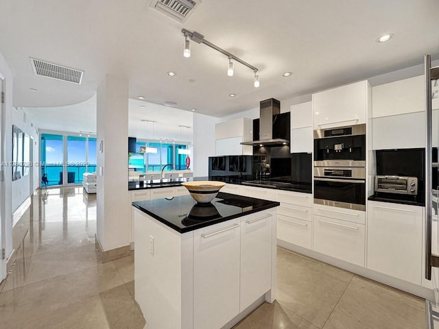 kitchen featuring a kitchen island, white cabinets, sink, and wall chimney range hood