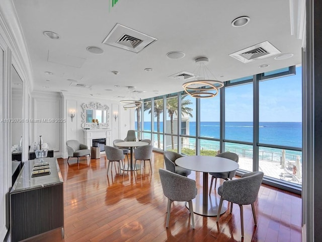 dining space featuring hardwood / wood-style floors, crown molding, a wall of windows, a water view, and a view of the beach