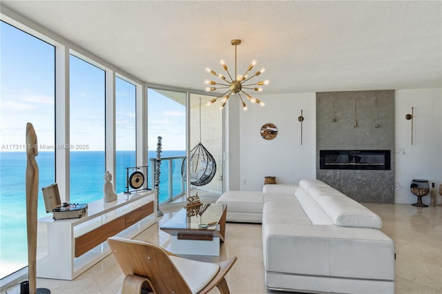 living room featuring a water view, floor to ceiling windows, a fireplace, a textured ceiling, and an inviting chandelier