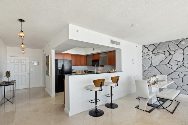 kitchen featuring kitchen peninsula, hanging light fixtures, a textured ceiling, a breakfast bar, and black appliances