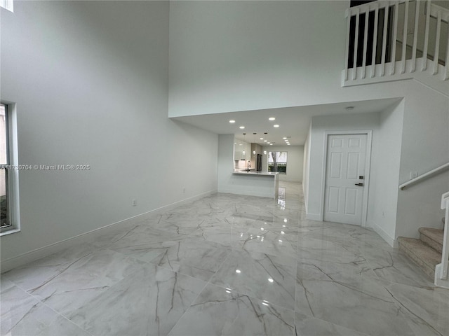 unfurnished living room with a high ceiling, marble finish floor, baseboards, and stairway
