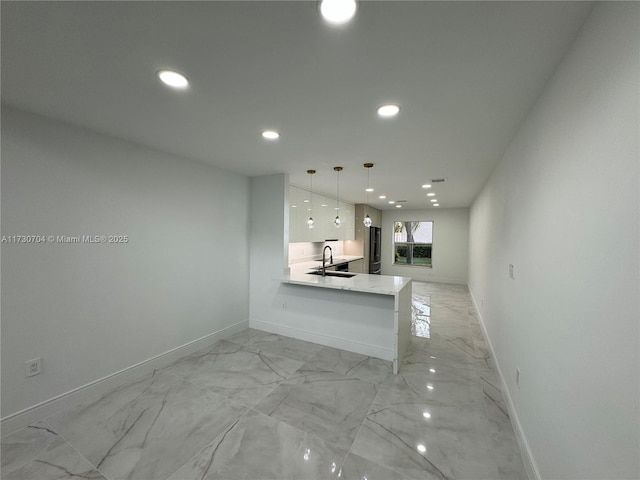 kitchen with marble finish floor, a sink, white cabinetry, and baseboards