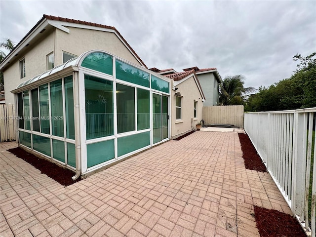 back of property featuring a sunroom, a tiled roof, a patio area, and stucco siding