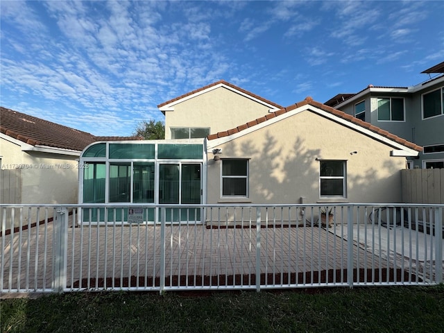 back of property with stucco siding, fence, and a tile roof