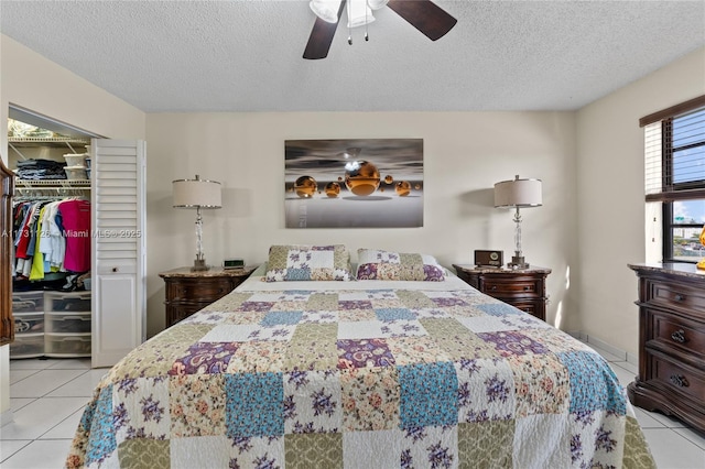 bedroom with a spacious closet, a textured ceiling, a closet, light tile patterned flooring, and ceiling fan