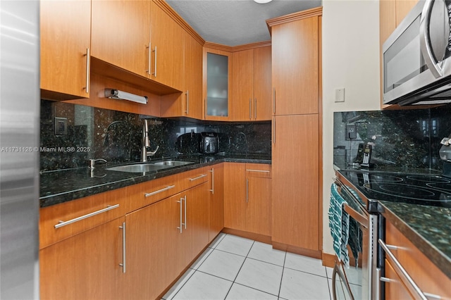 kitchen with appliances with stainless steel finishes, sink, light tile patterned flooring, dark stone countertops, and decorative backsplash