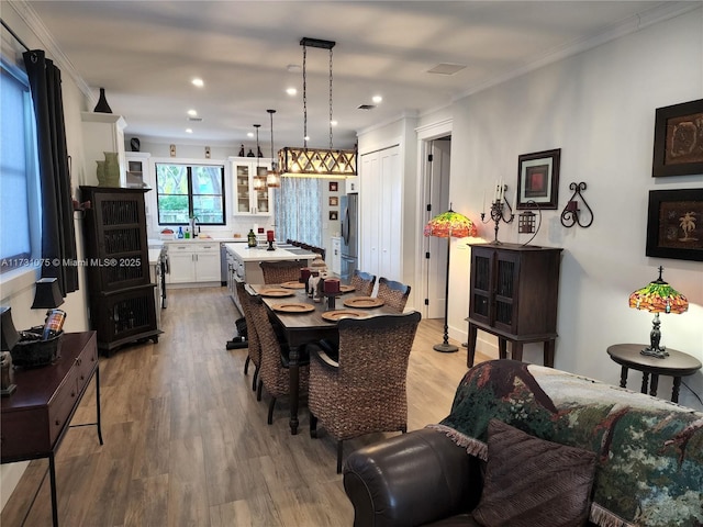 dining area featuring sink, light wood-type flooring, and ornamental molding