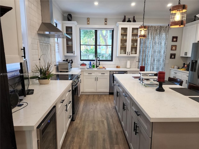 kitchen with hanging light fixtures, white cabinets, wall chimney range hood, and appliances with stainless steel finishes