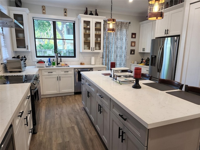 kitchen with appliances with stainless steel finishes, white cabinetry, decorative light fixtures, an island with sink, and light stone counters