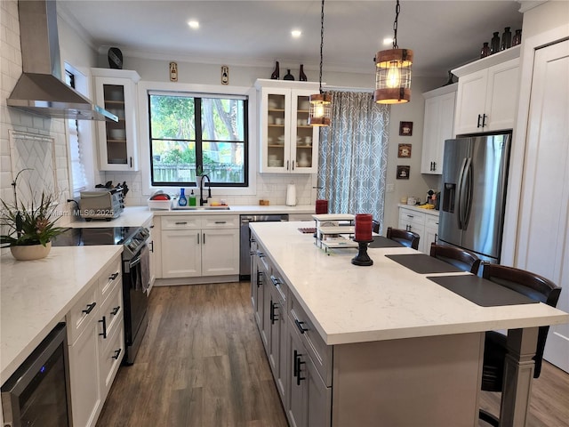 kitchen with wall chimney exhaust hood, white cabinets, a kitchen bar, and stainless steel appliances