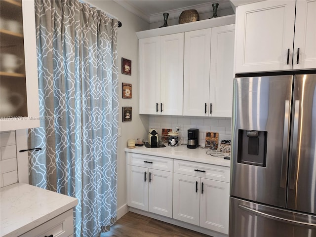 kitchen with light stone countertops, white cabinets, tasteful backsplash, stainless steel fridge, and crown molding