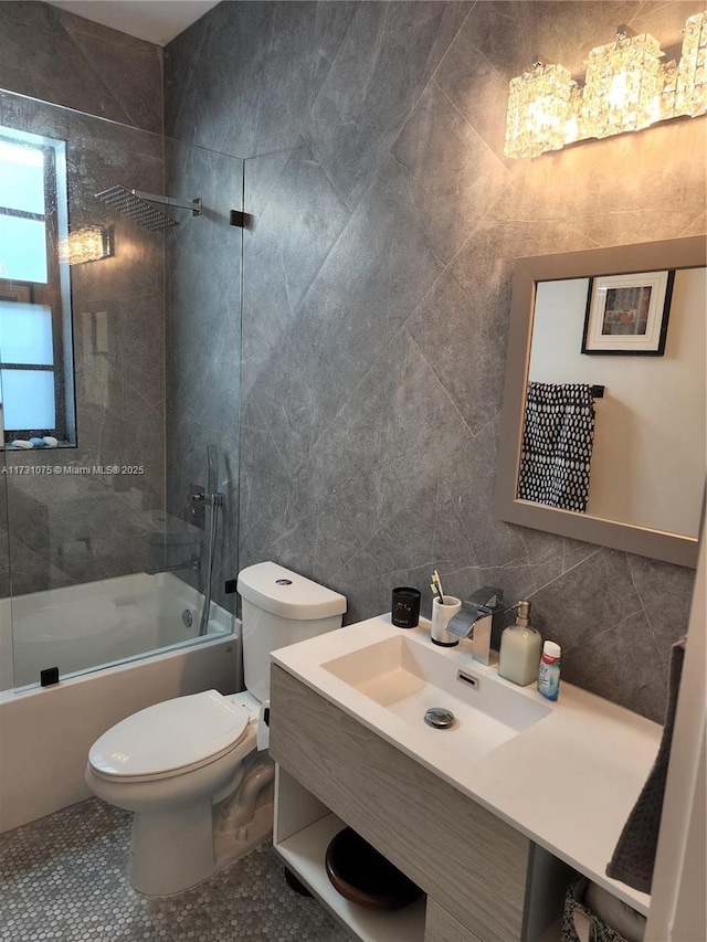 full bathroom with shower / bath combination with glass door, tile patterned floors, vanity, tile walls, and toilet