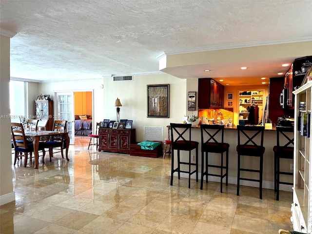 kitchen with visible vents, a breakfast bar area, a textured ceiling, and ornamental molding