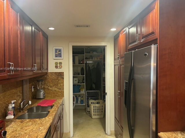 kitchen with sink, backsplash, light stone counters, and stainless steel refrigerator with ice dispenser