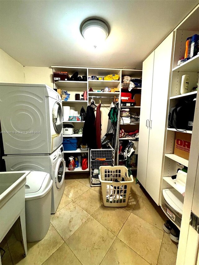 clothes washing area with sink, light tile patterned flooring, and stacked washer and clothes dryer