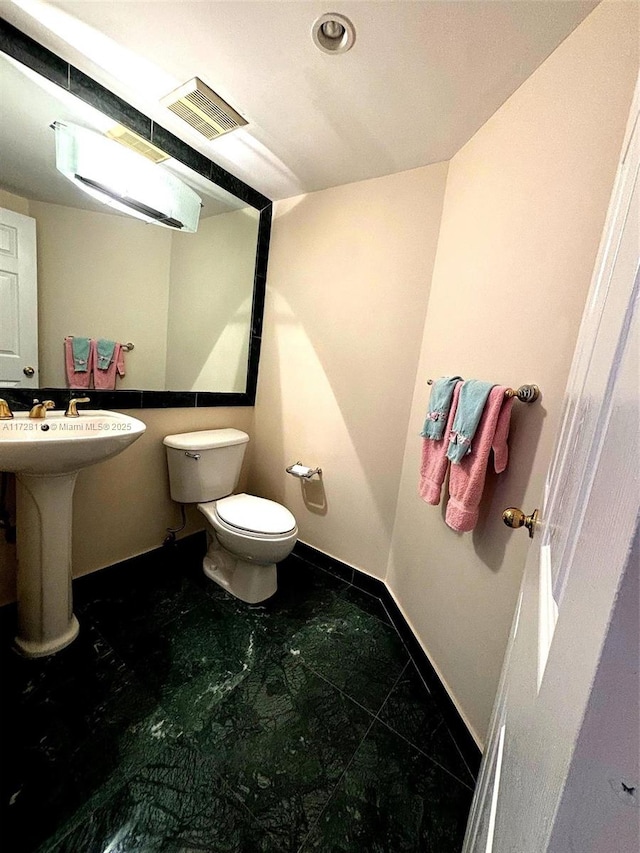 half bathroom featuring toilet, a sink, visible vents, and baseboards