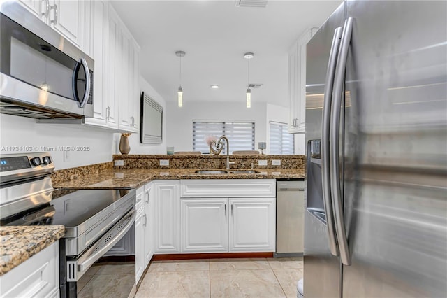 kitchen featuring white cabinetry, stainless steel appliances, dark stone counters, sink, and hanging light fixtures