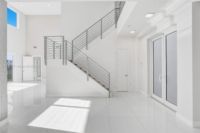 entrance foyer with french doors, a towering ceiling, a healthy amount of sunlight, and light tile patterned floors