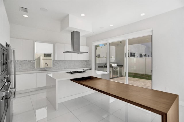 kitchen with island range hood, sink, white cabinets, light tile patterned floors, and gas cooktop