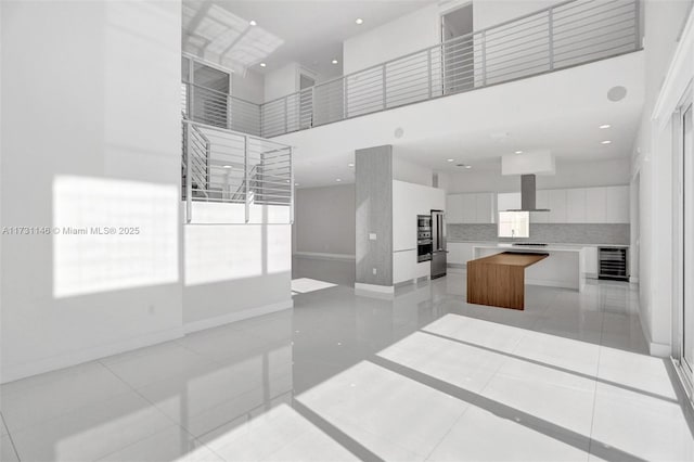 kitchen featuring wine cooler, extractor fan, white cabinetry, a towering ceiling, and a large island