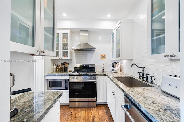 kitchen featuring wall chimney range hood, sink, stainless steel appliances, light stone countertops, and white cabinets