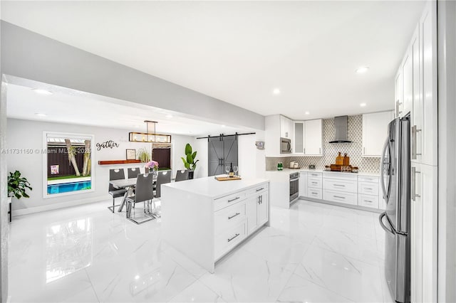 kitchen with stainless steel appliances, decorative backsplash, a barn door, wall chimney range hood, and marble finish floor