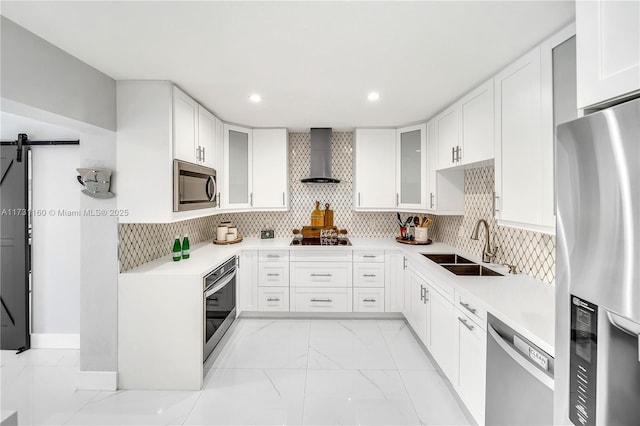 kitchen featuring a sink, appliances with stainless steel finishes, a barn door, wall chimney range hood, and marble finish floor