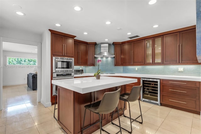 kitchen with a kitchen island, appliances with stainless steel finishes, beverage cooler, a kitchen breakfast bar, and wall chimney exhaust hood