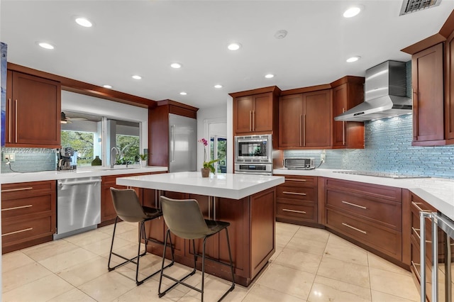 kitchen with a breakfast bar, appliances with stainless steel finishes, a kitchen island, decorative backsplash, and wall chimney range hood