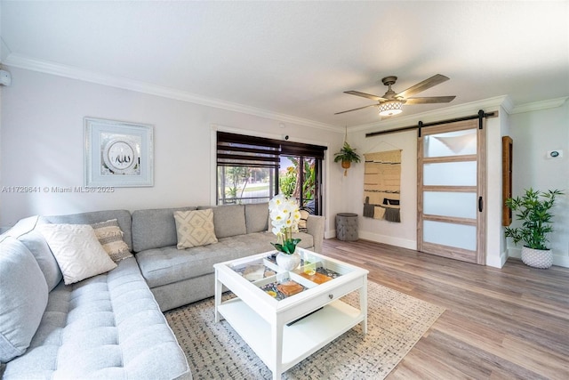 living room with light wood-type flooring, ceiling fan, a barn door, and crown molding