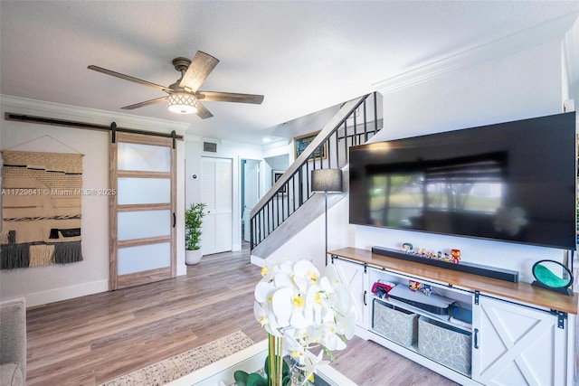 interior space with ceiling fan, light hardwood / wood-style flooring, crown molding, and a barn door