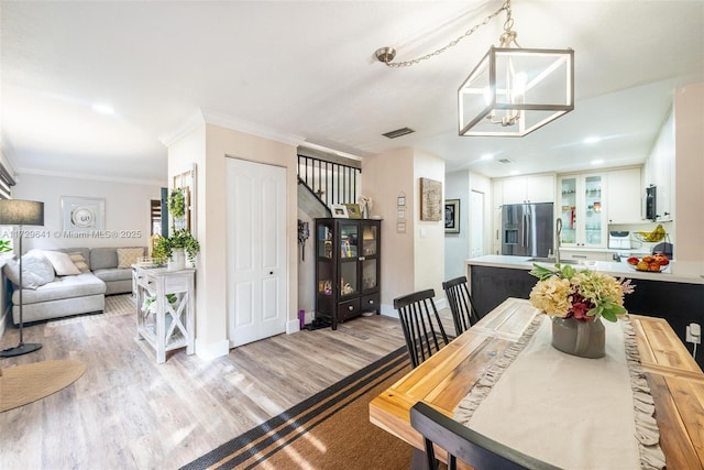 dining area featuring sink, ornamental molding, light hardwood / wood-style floors, and an inviting chandelier