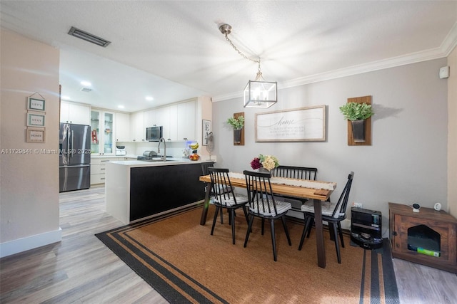 dining room featuring light hardwood / wood-style floors, sink, and ornamental molding